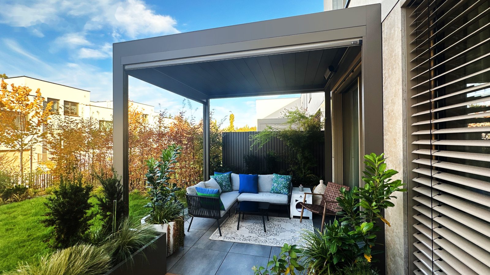Pergola bioclimatique adossée abritant un coin salon avec stores latéraux — Archimetal